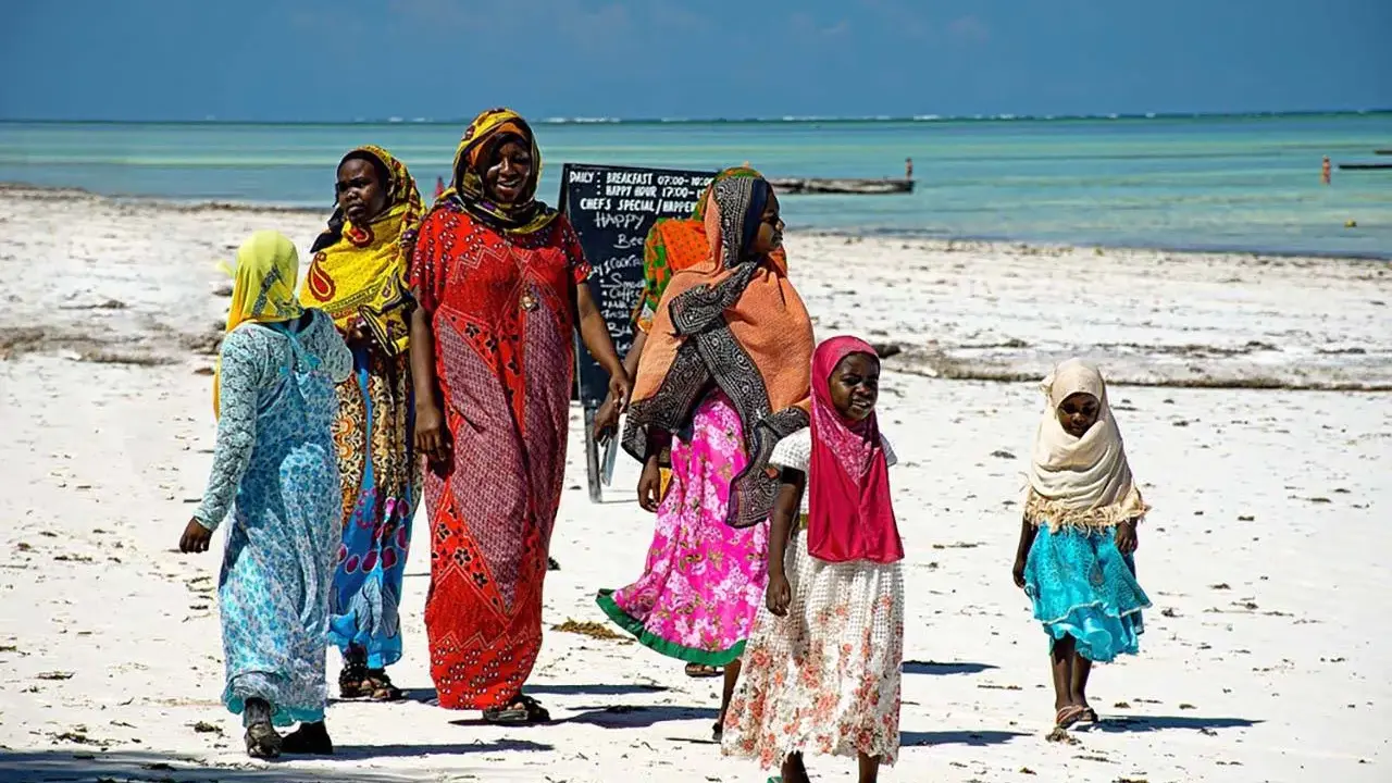 Kobiety w kolorowych strojach spacerują po plaży. Czy Zanzibar to kraj? Tak, to wyspa w Tanzanii.