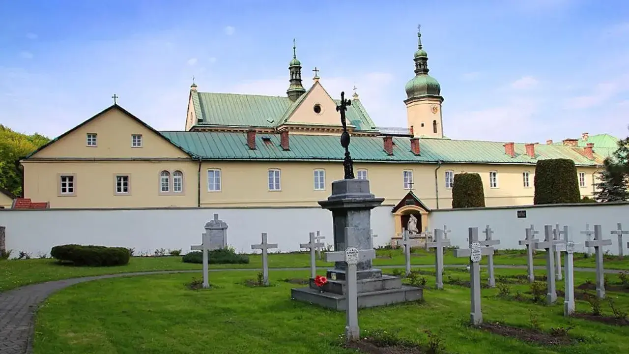 Cmentarz przy klasztorze w Czerniej. W tle żółty budynek z zielonym dachem i wieżą.
