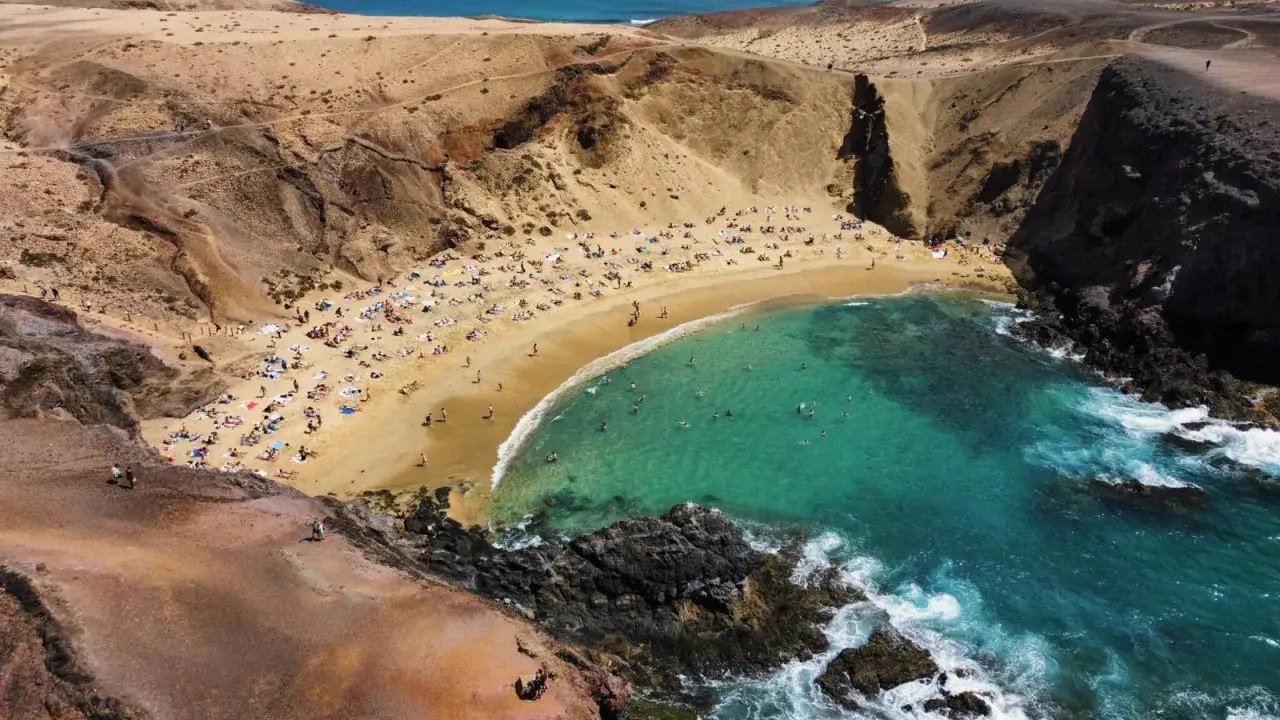 Rajska plaża z turkusową wodą i ludźmi opalającymi się na piasku. To idealne miejsce, co zobaczyć na Lanzarote, by poczuć słońce i odpocząć.