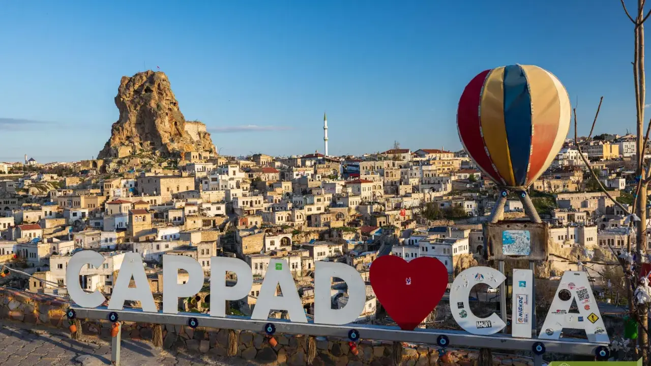 Cappadocia, Turcja zwiedzanie na własną rękę. Balon i napis "Cappadocia" na tle skalnych domów i twierdzy.