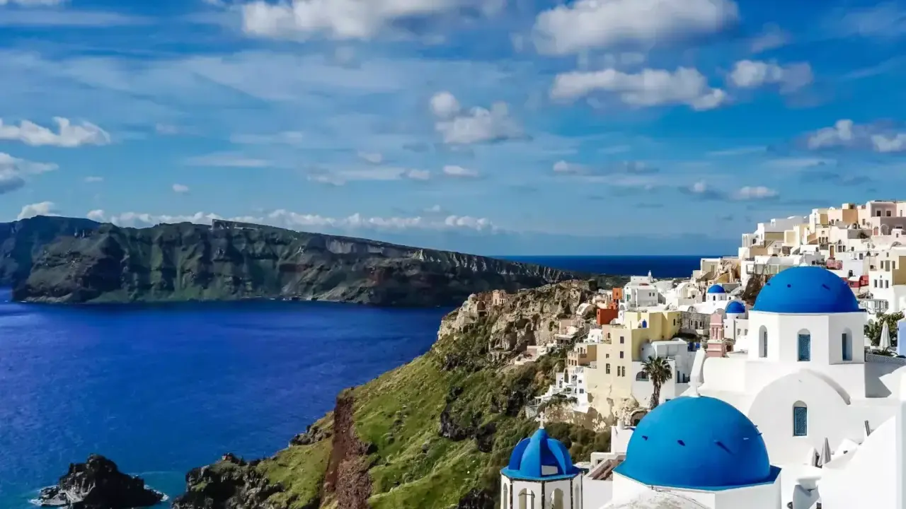 Widok na białe domy z niebieskimi kopułami na klifie, morze i góry. Klasyczny krajobraz Grecji, Santorini.