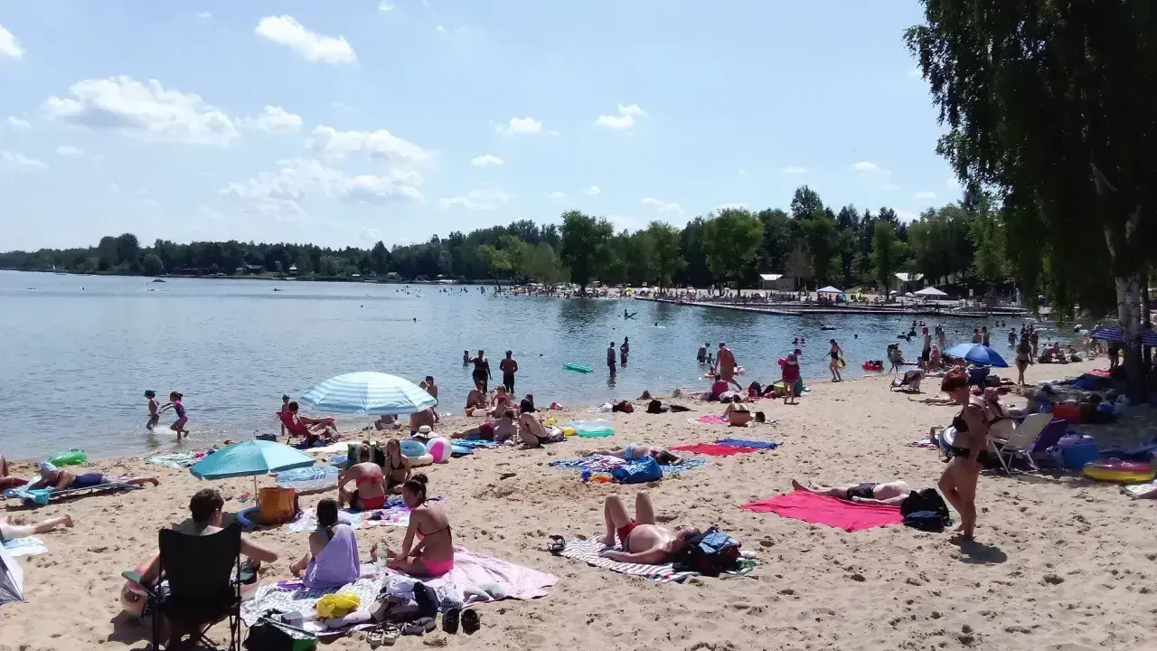 Słoneczny dzień nad **jaworznem jeziorem**. Ludzie odpoczywają na plaży, kąpią się i opalają.