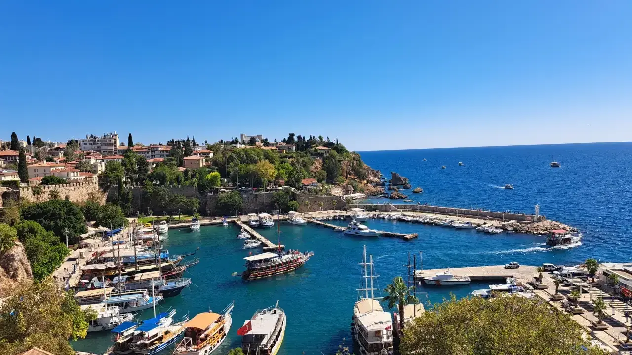 Widok na port w Antalyi, gdzie cumują liczne łodzie i jachty. W tle widać miasto i błękitne morze. Idealne miejsce, by zobaczyć, co oferuje Antalya.