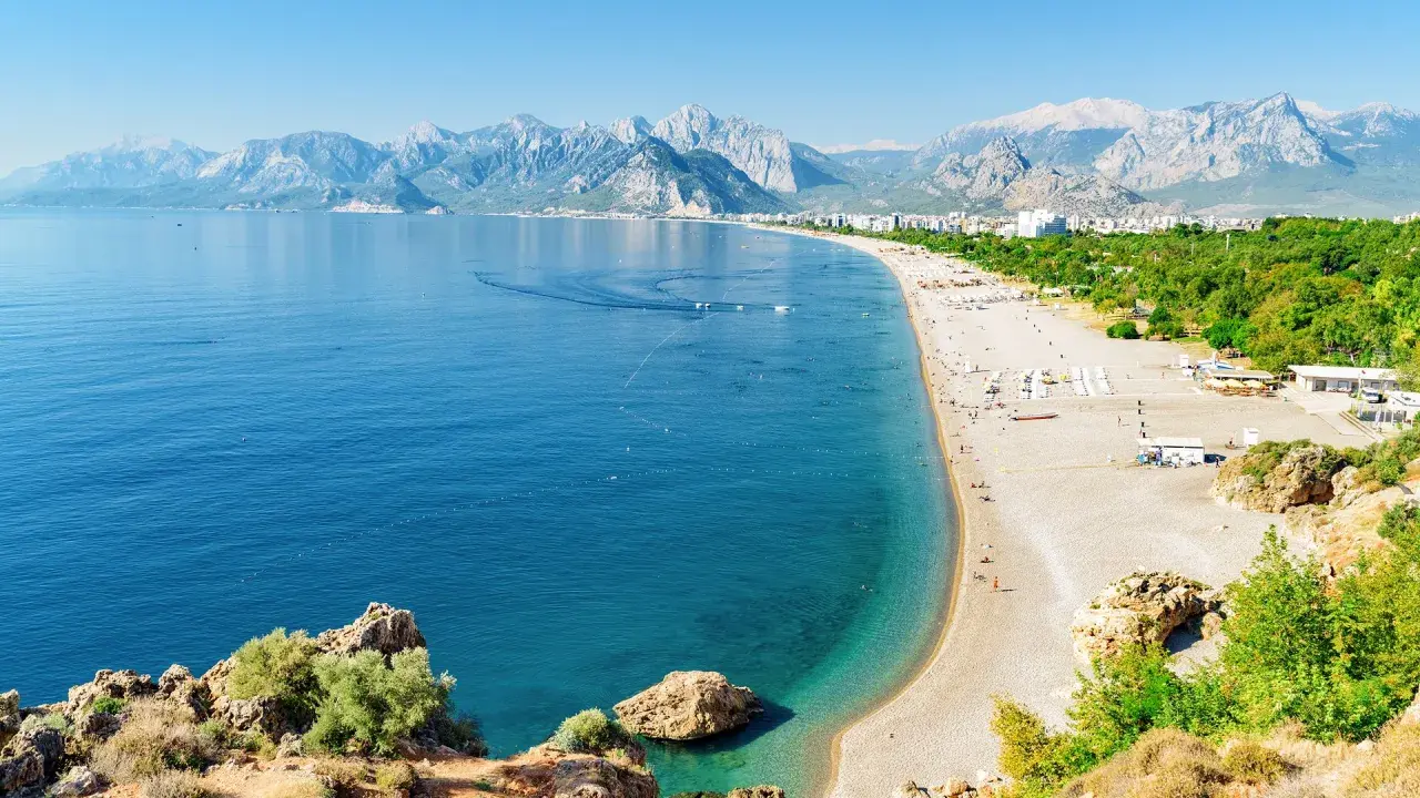 Słoneczna riwiera turecka Antalya kusi turkusowym morzem i piaszczystą plażą, w tle majestatyczne góry.