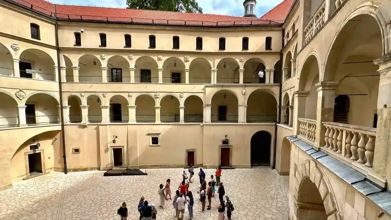 Dziedziniec zamku Ojcowie z arkadowymi krużgankami, gdzie spacerują turyści.