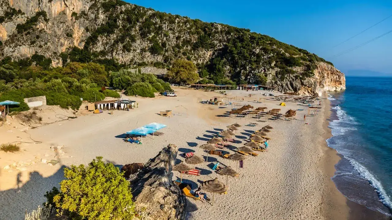 Piękne albania plaże z rzędami leżaków i parasoli, skaliste zbocze i turkusowe morze.