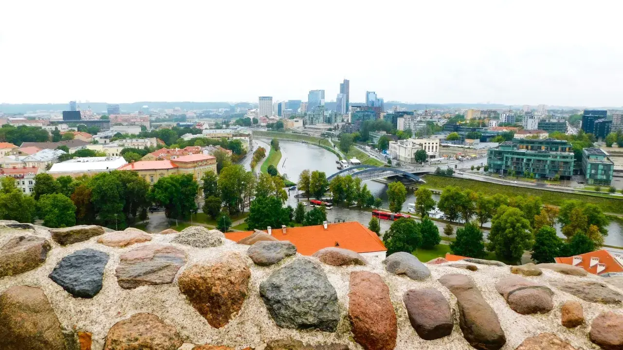 Widok na nowoczesne centrum Wilna z rzeką i mostami, a na pierwszym planie kamienny murek.