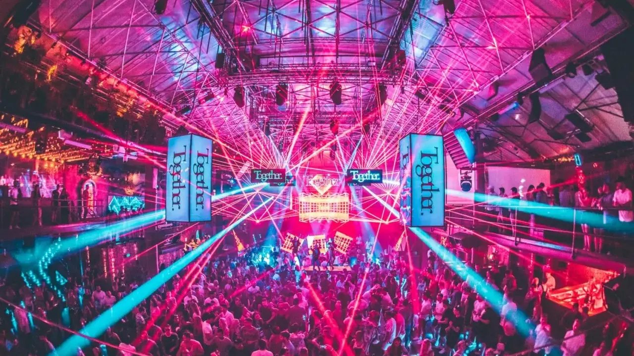 Tłum ludzi tańczy w rytm muzyki pod neonowymi światłami i laserami. To niezapomniane ibiza imprezy w klubie pełnym energii.