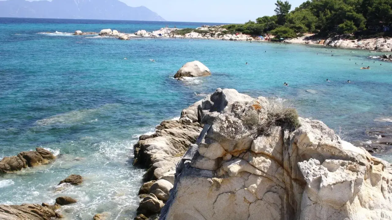 Piękne, turkusowe morze i skaliste wybrzeże. Ludzie kąpią się i opalają na plaży. To idealne chalkidiki atrakcje dla każdego.