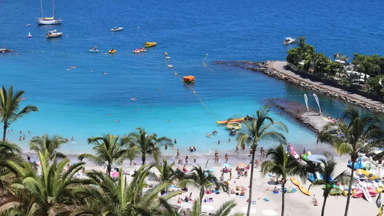 Słoneczne gran canaria plaże pełne ludzi, łodzi i palm. Błękitna woda zaprasza do kąpieli i wodnych zabaw.