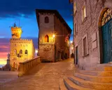 Kamienne uliczki i wieże w San Marino o zmierzchu, z kolorowym niebem i oświetlonymi budynkami.