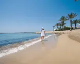 Dziewczyna w białej sukience i niebieskim kapeluszu spaceruje po piaszczystej plaży na Cyprze. Widok idealny, by zobaczyć, co oferuje wyspa.