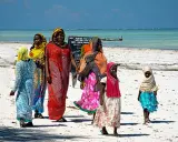 Kobiety w kolorowych strojach spacerują po plaży. Czy Zanzibar to kraj? Tak, to wyspa w Tanzanii.