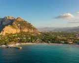 Malownicze **Palermo plaża** z turkusową wodą, skalistym klifem i miastem w tle.