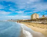 Słoneczna plaża w Golem, Albania, z rzędem leżaków i parasoli. W oddali widać hotel i miasto.