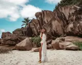 Kobieta w białej narzutce na plaży z granitowymi skałami w tle. Idealne miejsce na Seszele, co zobaczyć i poczuć.