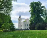 Biały zamek z niebieską kopułą, otoczony zielenią. Idealne miejsce na odkrywanie nietypowych atrakcji w Berlinie.