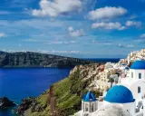 Widok na białe domy z niebieskimi kopułami na klifie, morze i góry. Klasyczny krajobraz Grecji, Santorini.