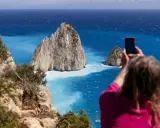 Widok na turkusowe morze i skaliste wysepki. Kobieta robi zdjęcie telefonem. Czy Zakynthos warto odwiedzić? Tak!
