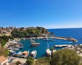 Widok na port w Antalyi, gdzie cumują liczne łodzie i jachty. W tle widać miasto i błękitne morze. Idealne miejsce, by zobaczyć, co oferuje Antalya.