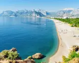 Słoneczna riwiera turecka Antalya kusi turkusowym morzem i piaszczystą plażą, w tle majestatyczne góry.