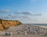 Plaża na wyspie Sylt z rzędem białych koszy plażowych i klifem w tle.