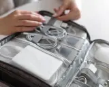 W torbie podróżnej schludnie ułożone kable, ładowarki i powerbank do samolotu. Dłonie porządkują zawartość.