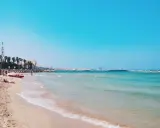 Słoneczna bari plaża z turkusową wodą i palmami w tle. Czerwona łódź ratownicza na piasku.