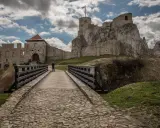 Kamienny most prowadzi do ruin zamku w Olkuszu. Na szczycie skalistego wzgórza widać wieżę z polską flagą.