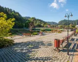 Słoneczna promenada Szczawnica z kamienną nawierzchnią, ławkami i latarniami, otoczona zielenią i górami.