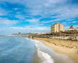 Słoneczna plaża w Durrës, Albania, z rzędami leżaków i parasoli. W tle widać hotel i miasto, a na pierwszym planie falujące morze. Idealne miejsce na wakacje i odkrywanie atrakcji.