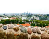 Widok na nowoczesne centrum Wilna z rzeką i mostami, a na pierwszym planie kamienny murek.