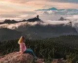 Kobieta siedzi na skale, podziwiając mgły i góry na Gran Canarii. W oddali widać Roque Nublo.