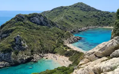 Malownicze zatoczki z turkusową wodą i piaszczystymi plażami na wyspie Korfu, otoczone zielonymi wzgórzami.
