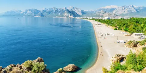 Słoneczna riwiera turecka Antalya kusi turkusowym morzem i piaszczystą plażą, w tle majestatyczne góry.