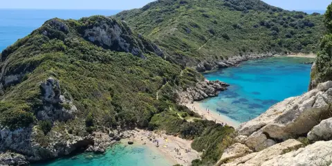 Malownicze zatoczki z turkusową wodą i piaszczystymi plażami na wyspie Korfu, otoczone zielonymi wzgórzami.