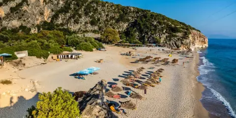 Piękne albania plaże z rzędami leżaków i parasoli, skaliste zbocze i turkusowe morze.