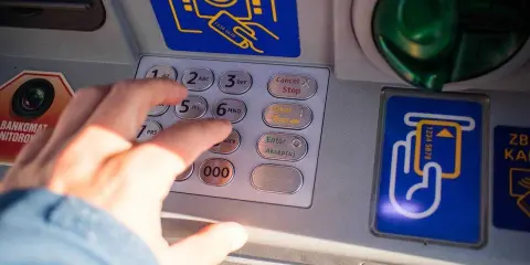 Dłoń wpisuje PIN na bankomacie w Turcji. Szukaj bankomatów bez prowizji, by oszczędzić na wakacjach.