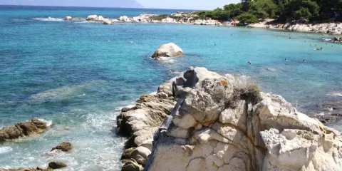 Piękne, turkusowe morze i skaliste wybrzeże. Ludzie kąpią się i opalają na plaży. To idealne chalkidiki atrakcje dla każdego.