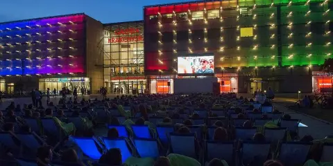 Wieczorny seans pod gołym niebem przed Galerią Krakowską. Tłum widzów w leżakach ogląda film na wielkim ekranie.