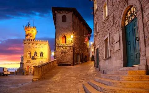 Kamienne uliczki i wieże w San Marino o zmierzchu, z kolorowym niebem i oświetlonymi budynkami.