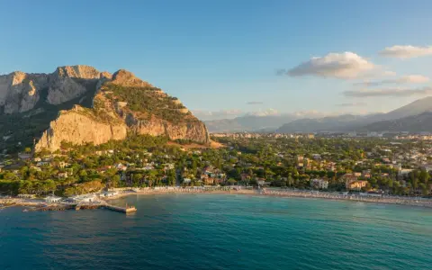 Malownicze **Palermo plaża** z turkusową wodą, skalistym klifem i miastem w tle.