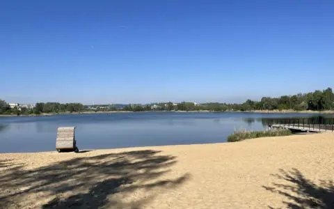 Plaża bagry z drewnianą przebieralnią i pomostem, w tle jezioro i zieleń.