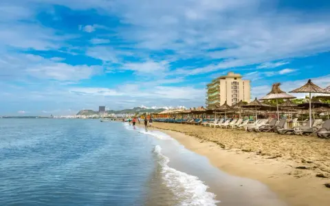 Słoneczna plaża w Golem, Albania, z rzędem leżaków i parasoli. W oddali widać hotel i miasto.
