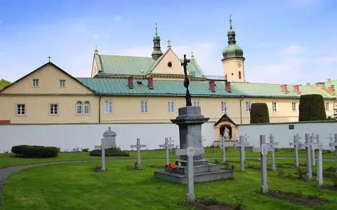 Cmentarz przy klasztorze w Czerniej. W tle żółty budynek z zielonym dachem i wieżą.