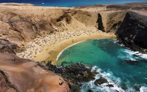 Rajska plaża z turkusową wodą i ludźmi opalającymi się na piasku. To idealne miejsce, co zobaczyć na Lanzarote, by poczuć słońce i odpocząć.