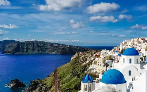 Widok na białe domy z niebieskimi kopułami na klifie, morze i góry. Klasyczny krajobraz Grecji, Santorini.