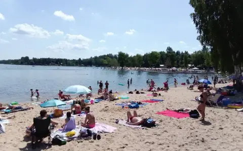 Słoneczny dzień nad **jaworznem jeziorem**. Ludzie odpoczywają na plaży, kąpią się i opalają.