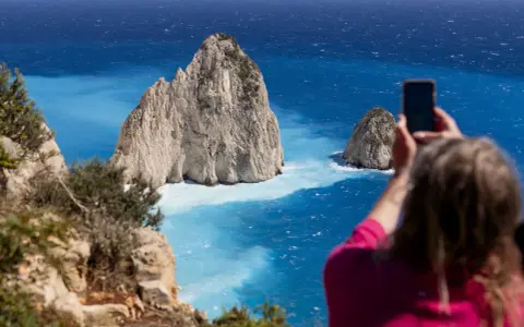 Widok na turkusowe morze i skaliste wysepki. Kobieta robi zdjęcie telefonem. Czy Zakynthos warto odwiedzić? Tak!