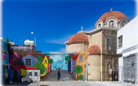 Kolorowy mural z rowerzystą i domkami na tle kościoła z kopułami. Pafos Cypr centrum.